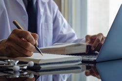 medical professional writing in a journal while at a laptop