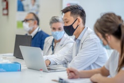 A group of doctors looking at a laptop in a classroom setting