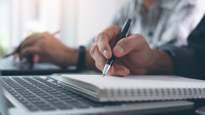 Person writing in notepad with pen