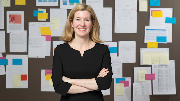 Headshot of Dr. Moira Kapral standing in her office in front of a colorful wall of notes and papers