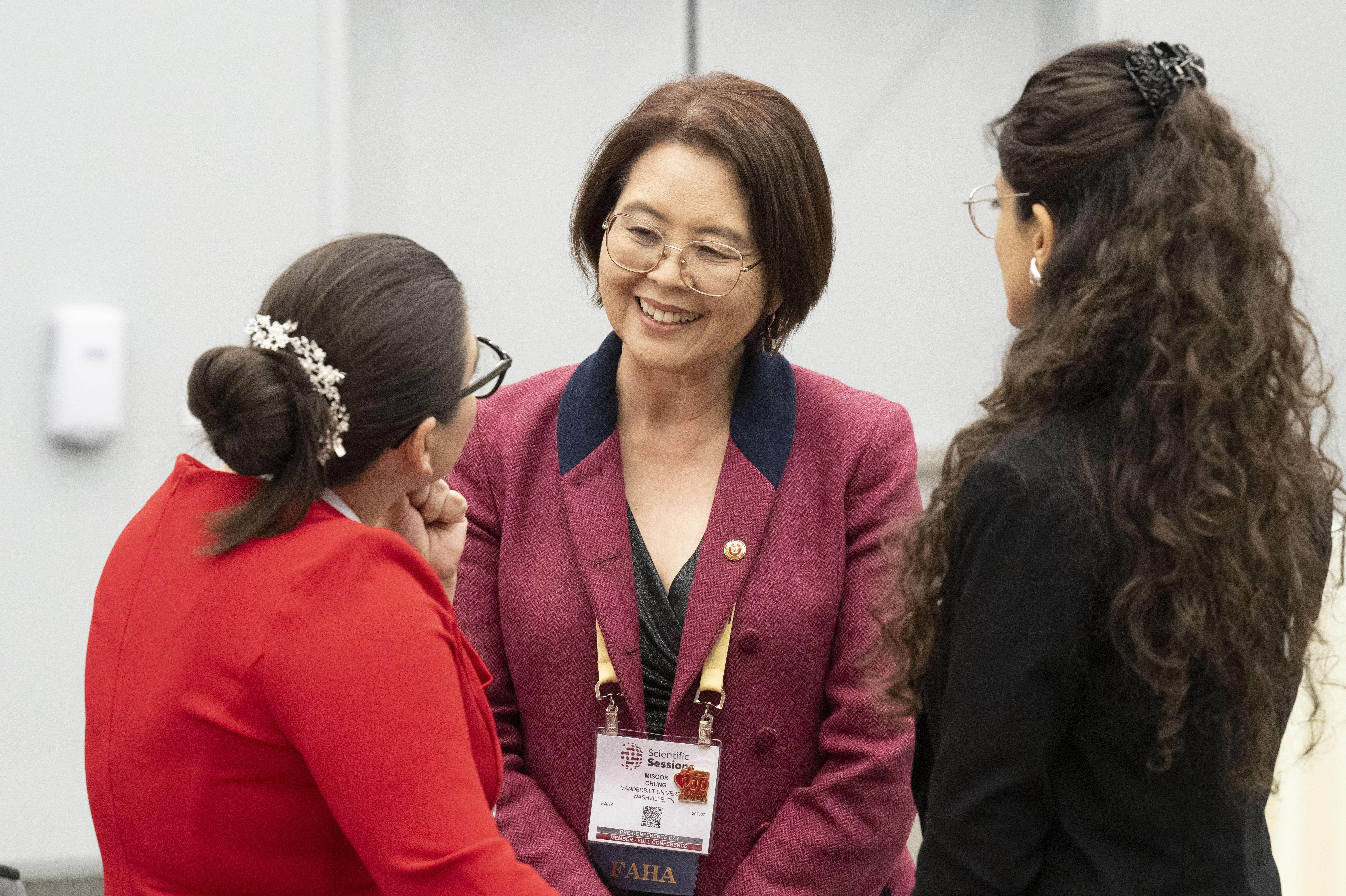 Smiling professional woman in burgundy blazer conversing with colleagues at conference