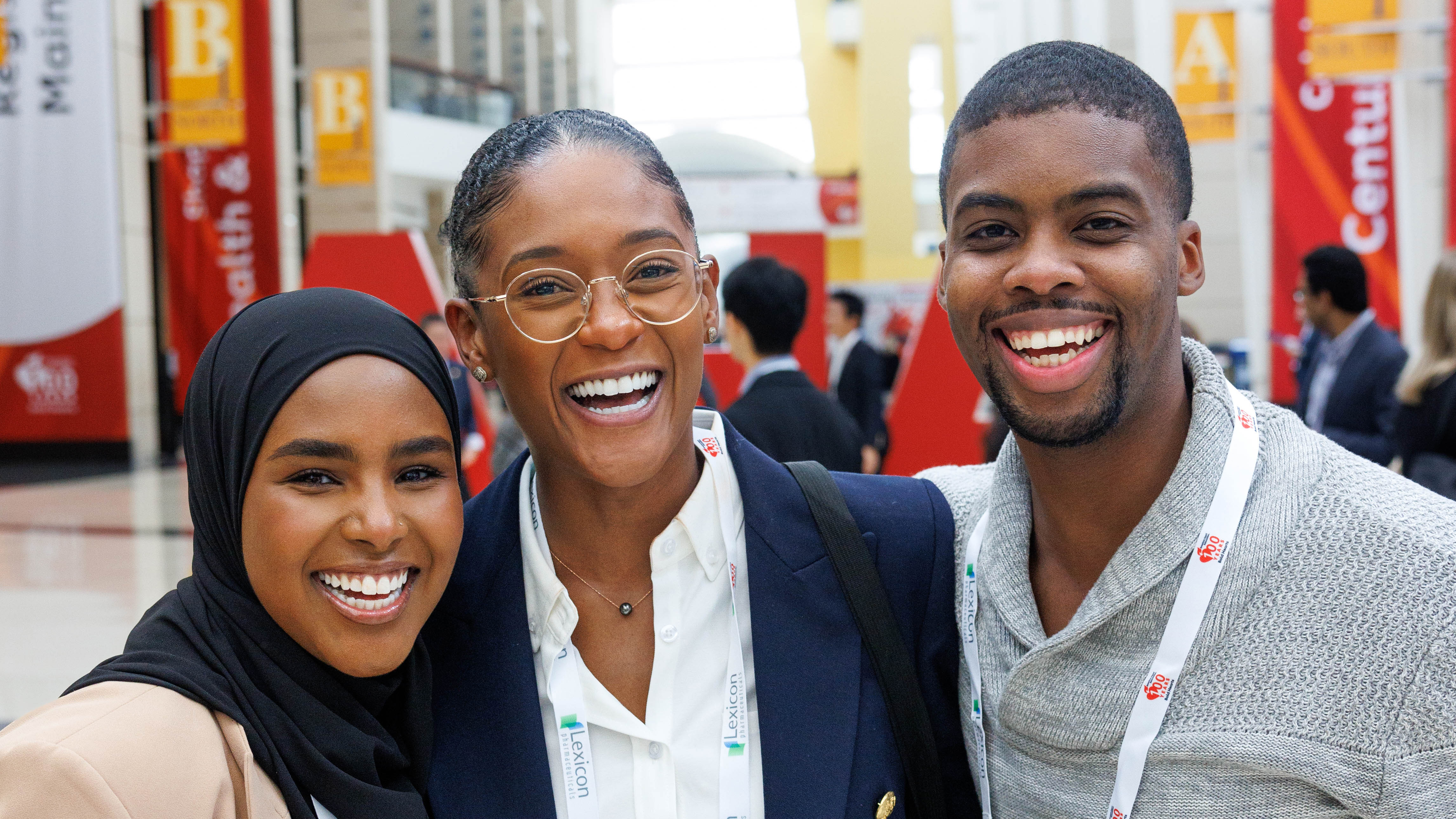 Three diverse professionals smiling together at conference with red signage