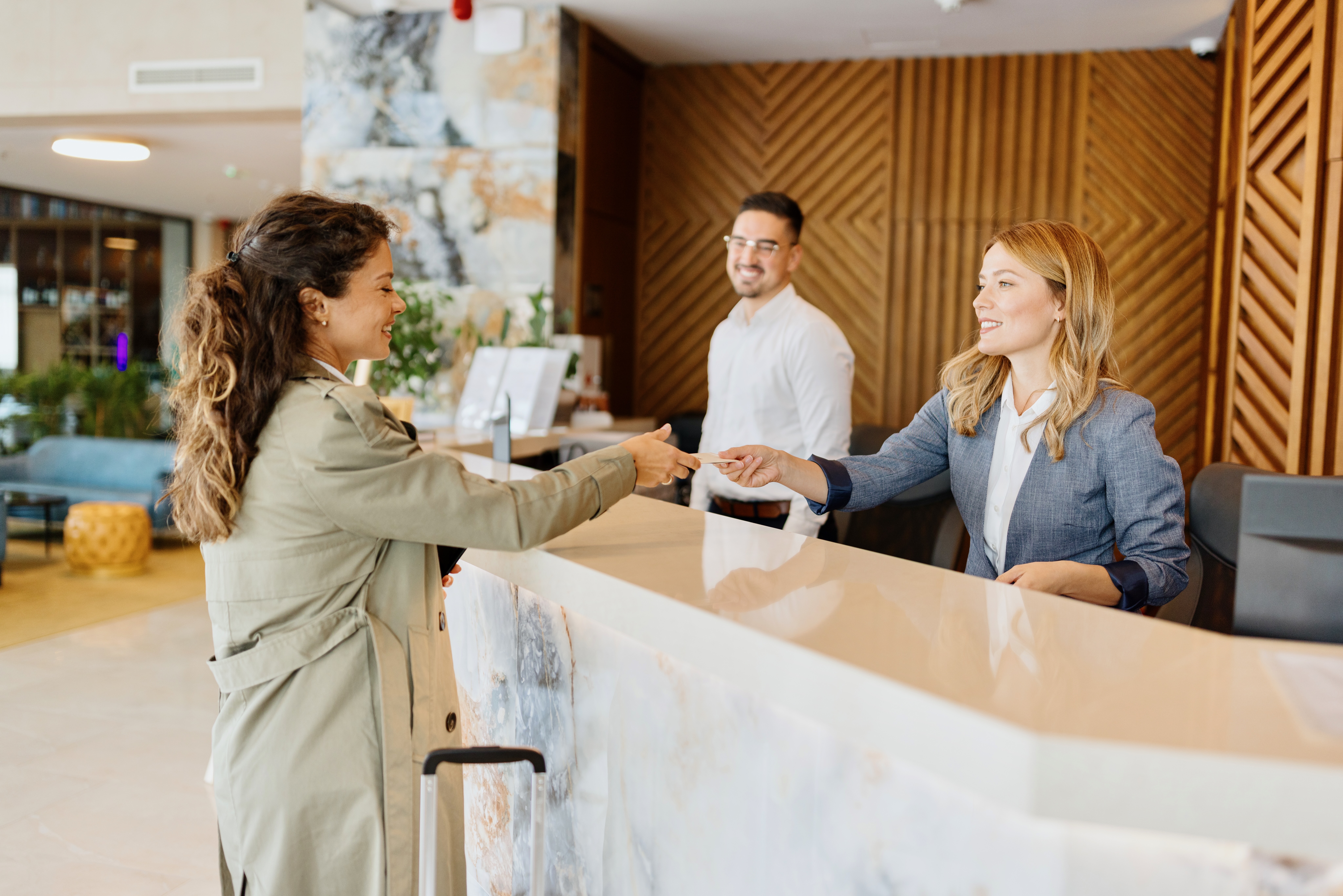 Hotel reception desk with staff greeting a traveler with luggage