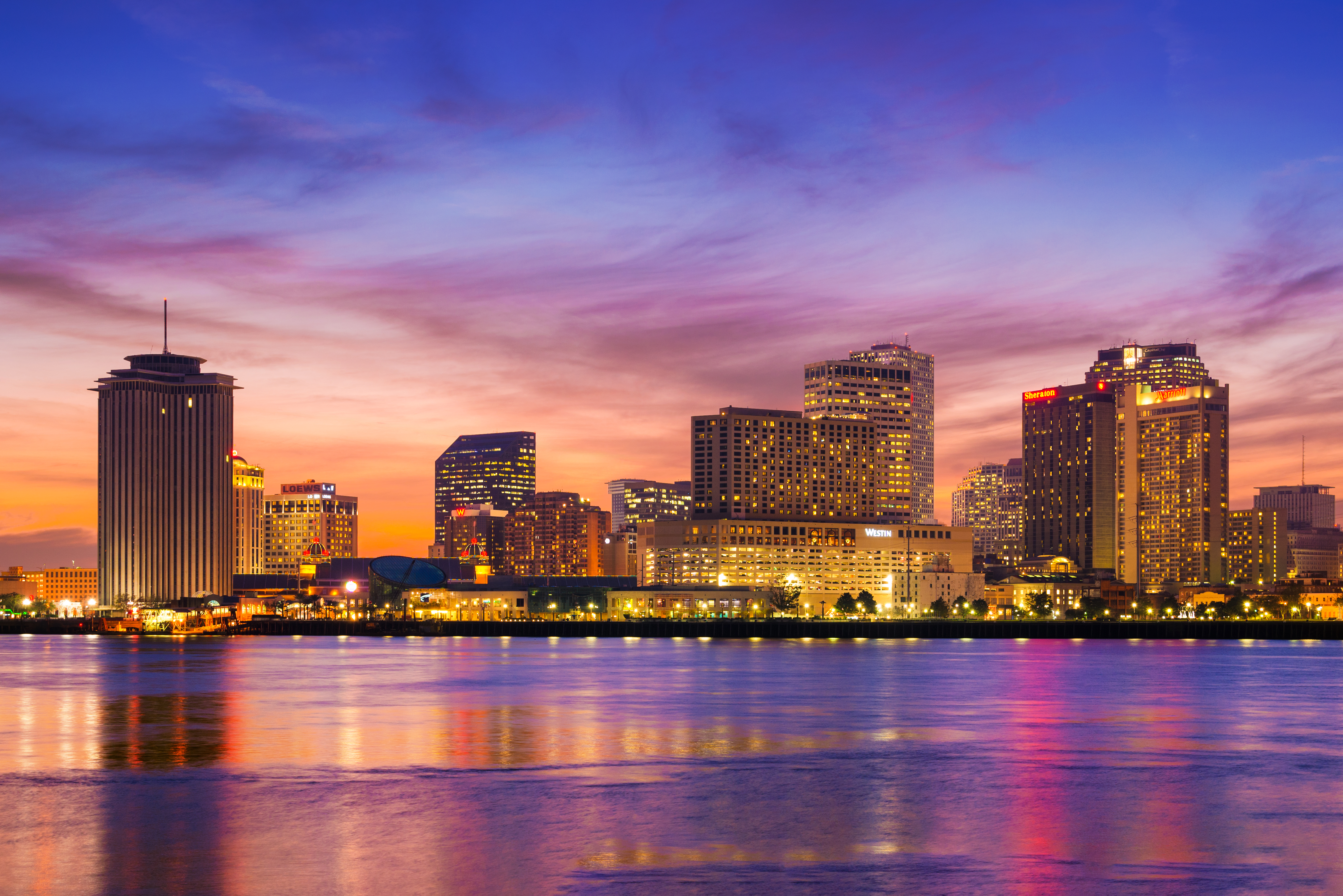 New Orleans skyline at sunset with colorful sky and Mississippi River reflection