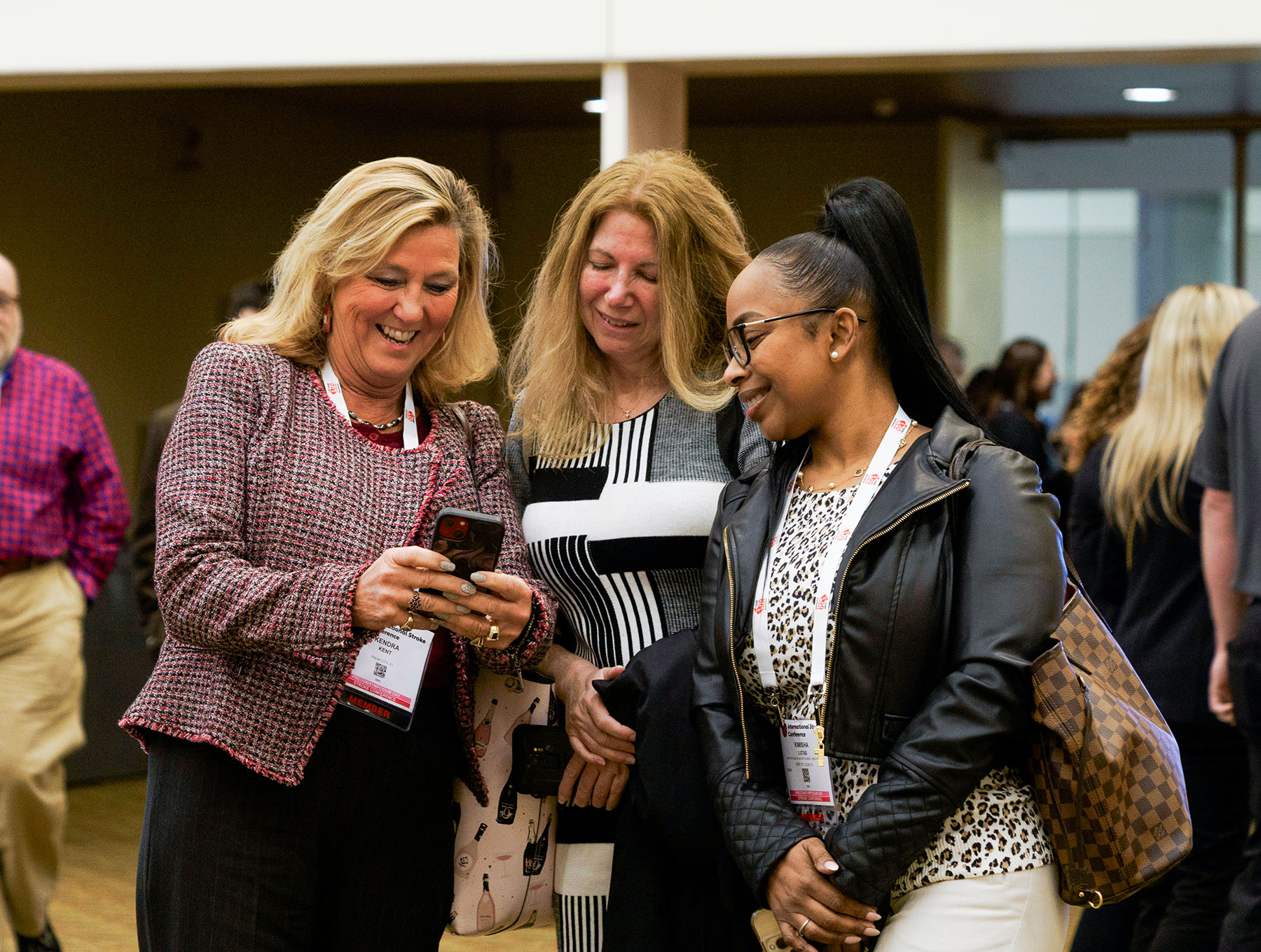 Three professional women smiling and looking at a smartphone during a conference