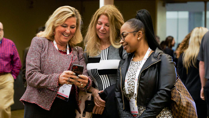 Three professional women smiling and looking at a smartphone during a conference