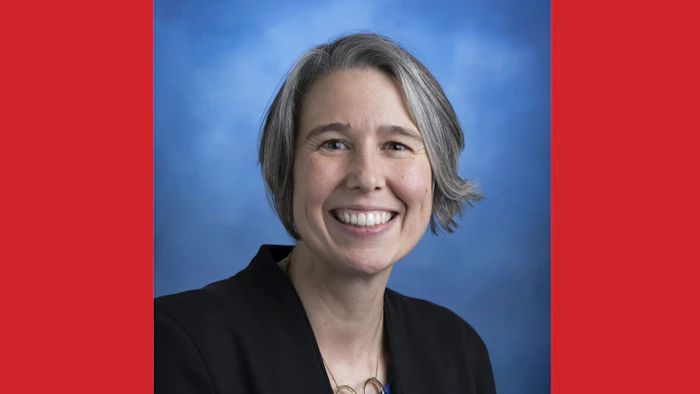 Professional woman smiling, wearing black blazer against blue background