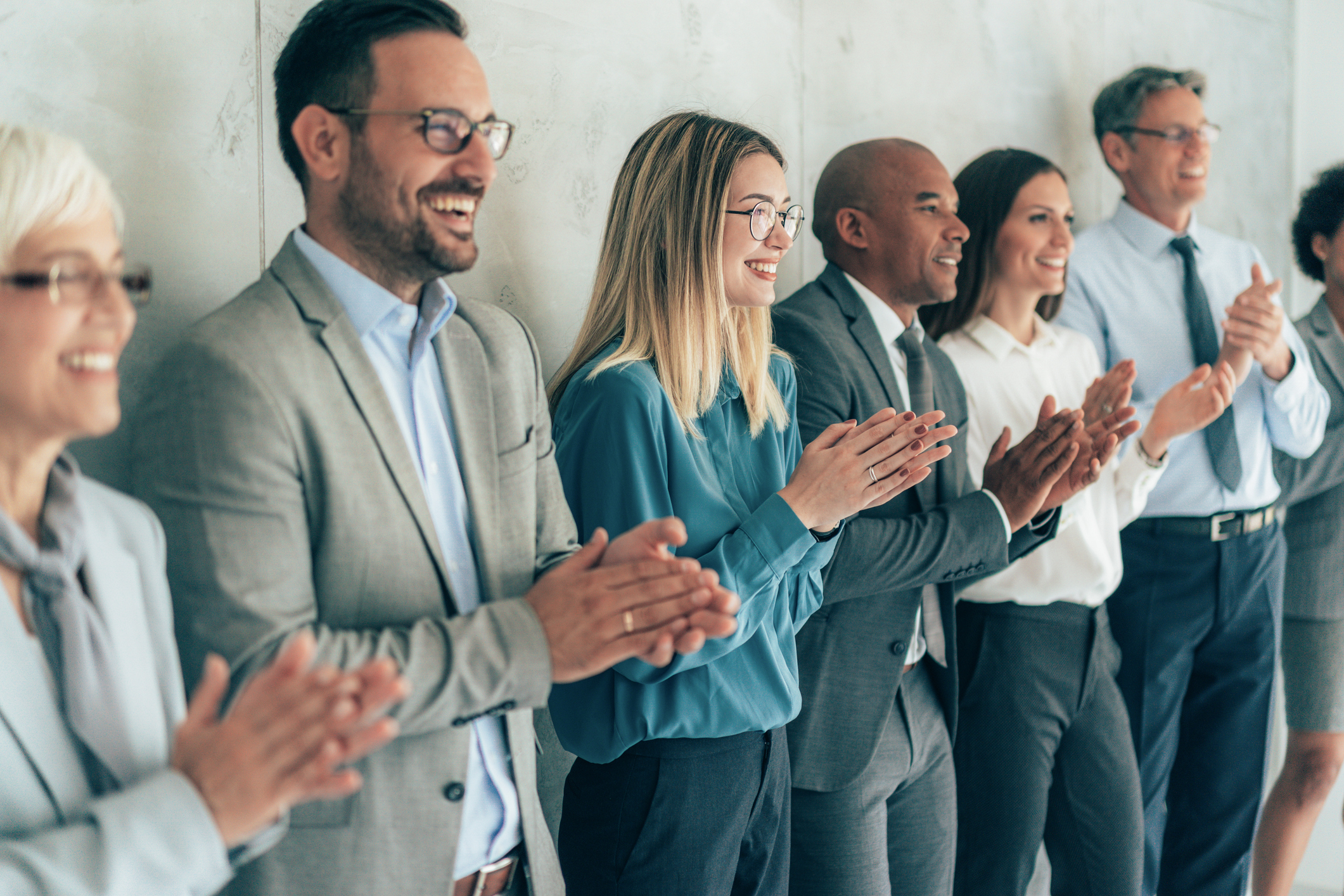 Diverse group of business professionals applauding and smiling in a modern office setting