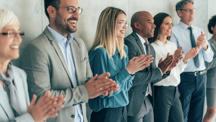 Diverse group of business professionals applauding and smiling in a modern office setting