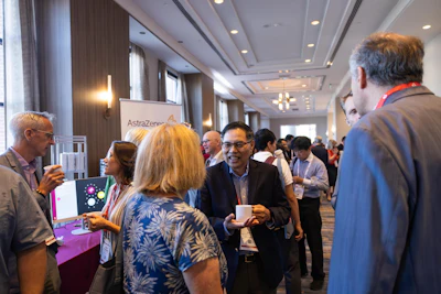 Professionals networking at a corporate conference event with AstraZeneca branding visible in the background.