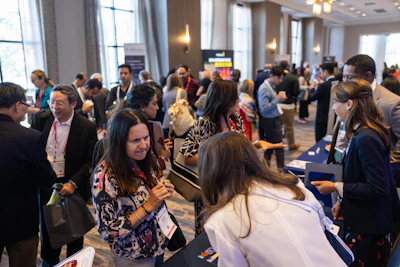Professionals networking at a crowded indoor conference event in a modern venue with large windows and contemporary lighting.