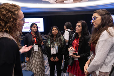 Group of professionals networking at a conference event, wearing badges and business attire in a modern venue.
