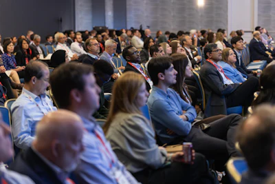 Large audience of attendees seated in an auditorium during a corporate conference or seminar event.