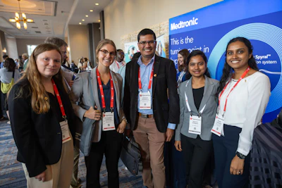 Five professionals smiling at Medtronic conference event with branded blue backdrop and ID badges