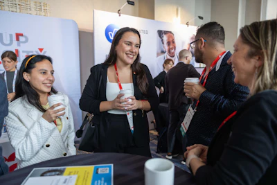 Professionals networking at a corporate conference, holding beverages and smiling while engaged in conversation at an event.