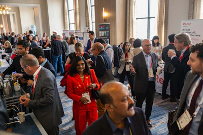 Professionals networking at a conference event with attendees wearing badges and business attire in a hotel ballroom.