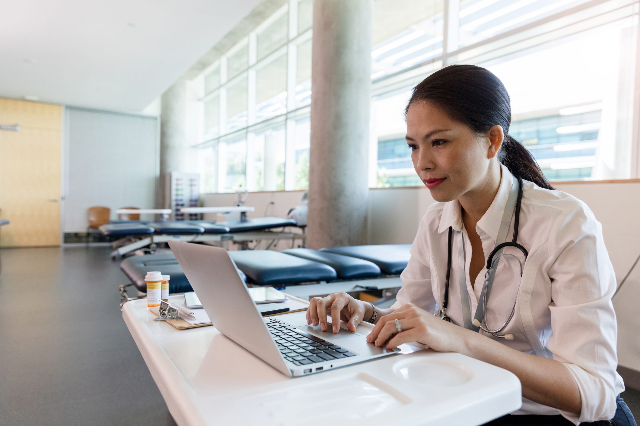 Female healthcare professional using laptop at desk in medical clinic with stethoscope