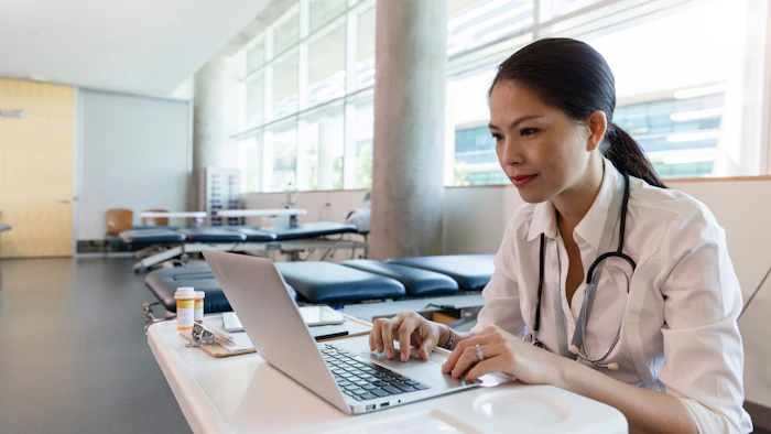 Female healthcare professional using laptop at desk in medical clinic with stethoscope