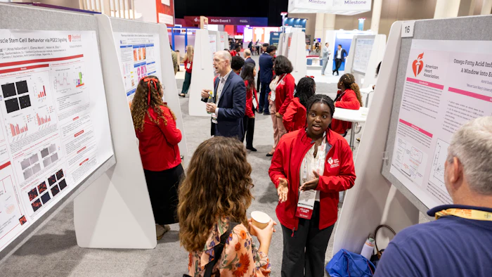 Researchers present medical posters at a conference with attendees in red jackets networking in a large venue.