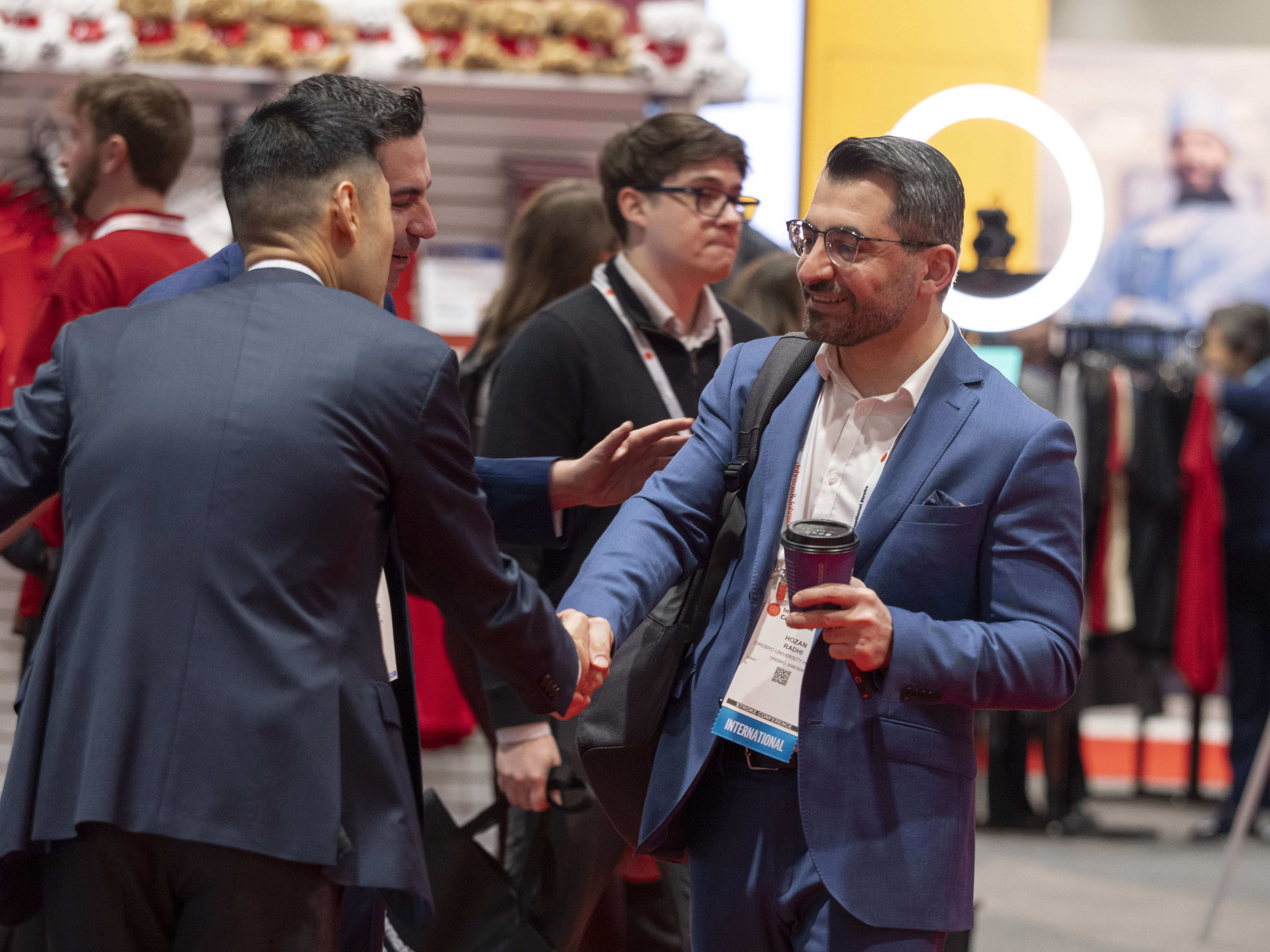 Professionals networking at a business conference, with attendees wearing ID badges and business suits engaged in conversation.