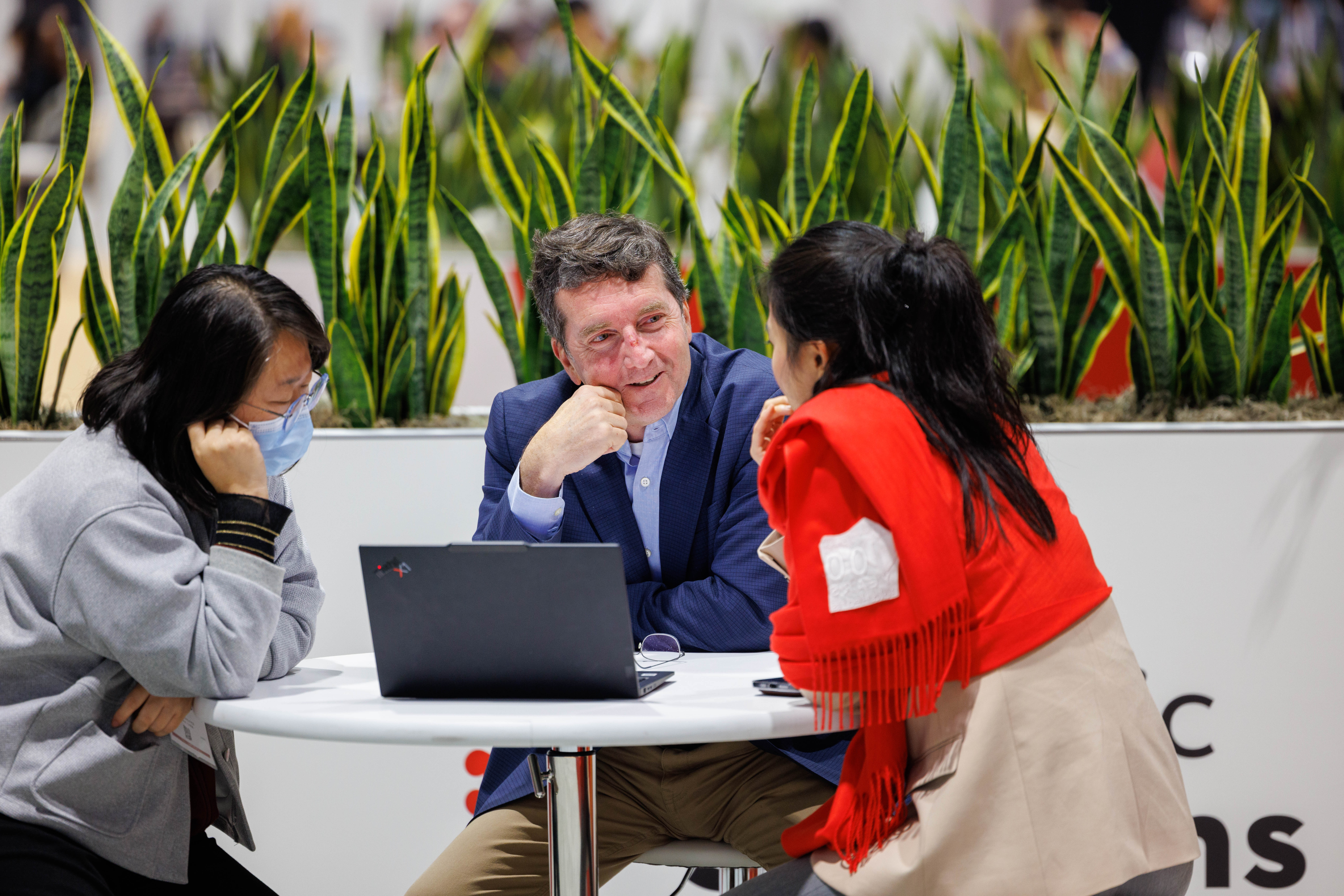 Three professionals discussing business strategy around a laptop during a meeting at a modern office workspace.