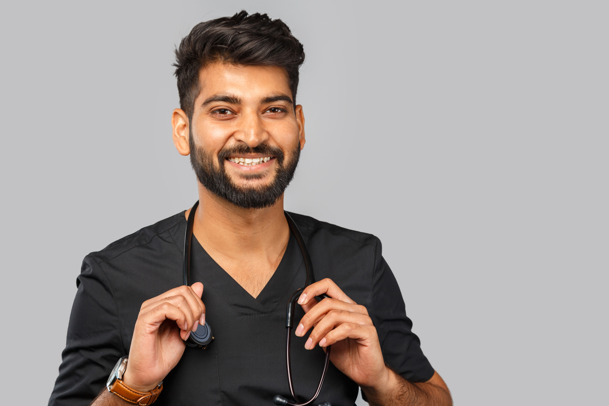Professional headshot of a smiling man in black v-neck shirt holding a stethoscope