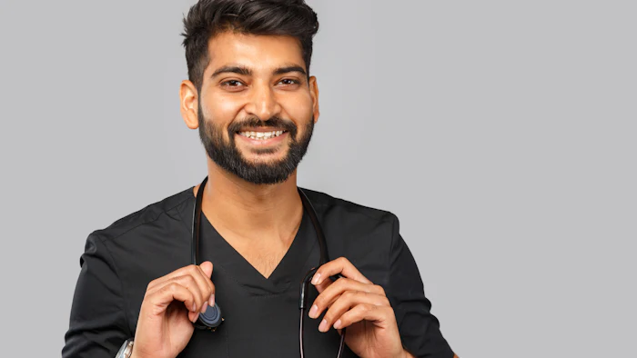 Professional headshot of a smiling man in black v-neck shirt holding a stethoscope