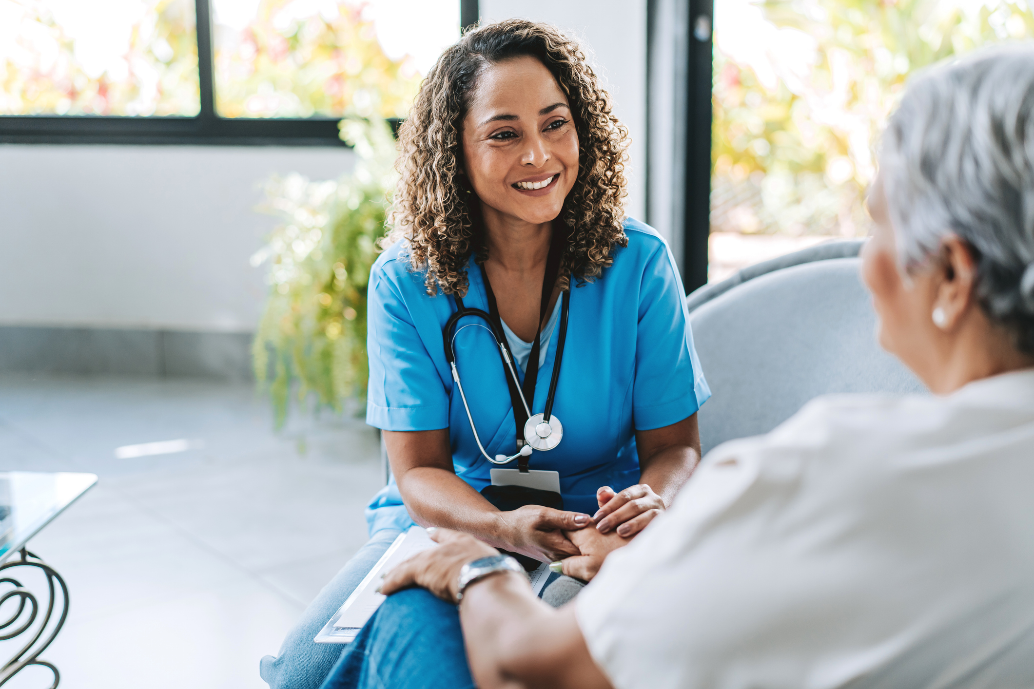 Female nurse in blue scrubs smiling while consulting with an elderly patient in a bright clinical setting