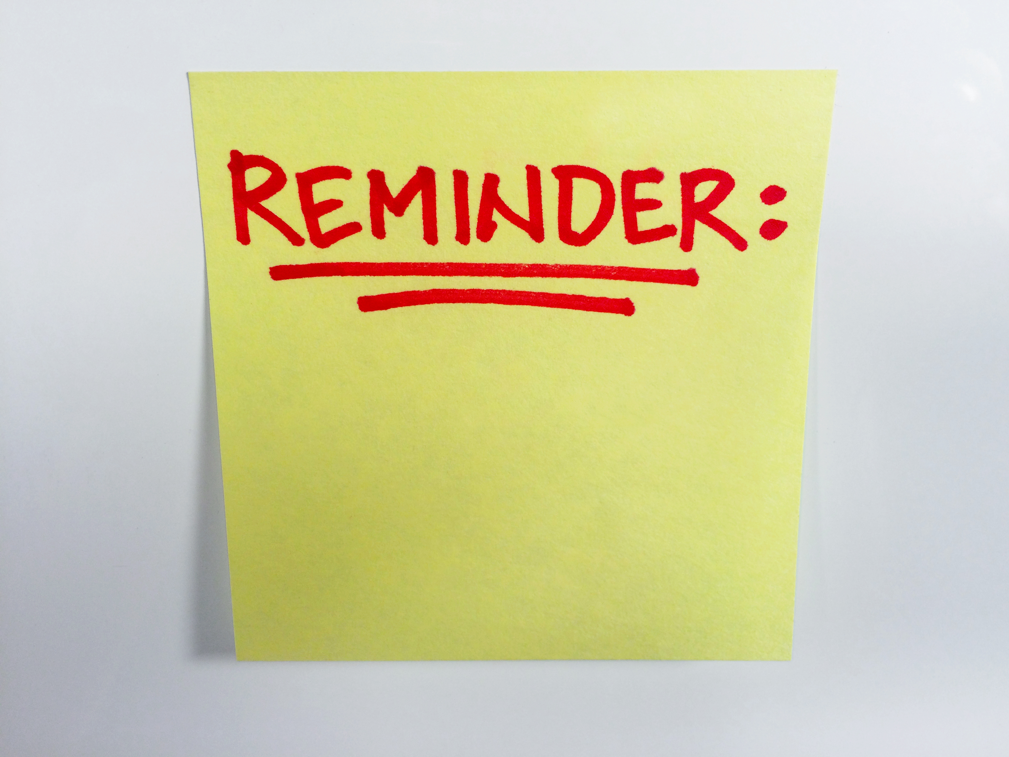 Yellow sticky note with red handwritten text reading 'REMINDER:' with an underline