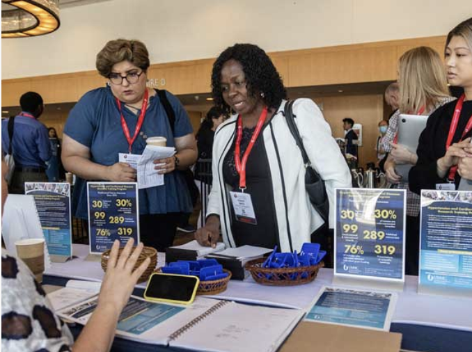 Conference attendees at an information booth discussing program statistics and materials